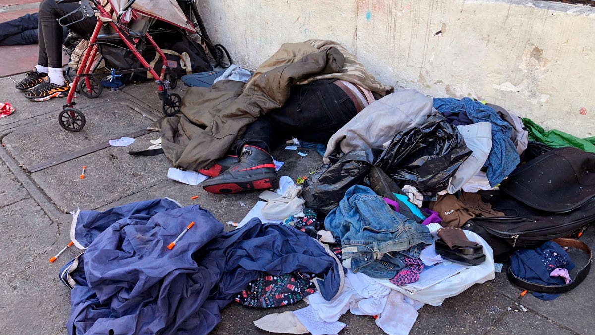 Homeless people sleeping on the sidewalk in a pile of discarded clothes and needles