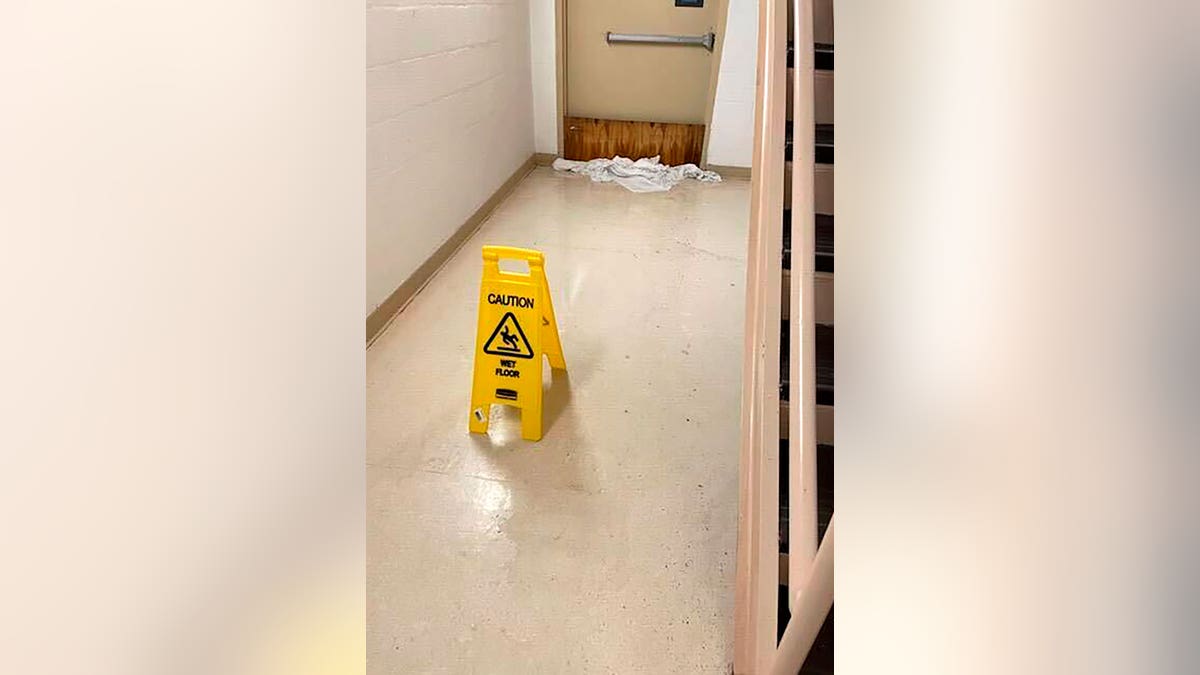 Water in the hallway with a caution sign and towels at the base of a door