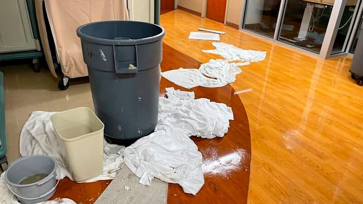 Trash can collecting dripping water from ceiling next to towels on the floor