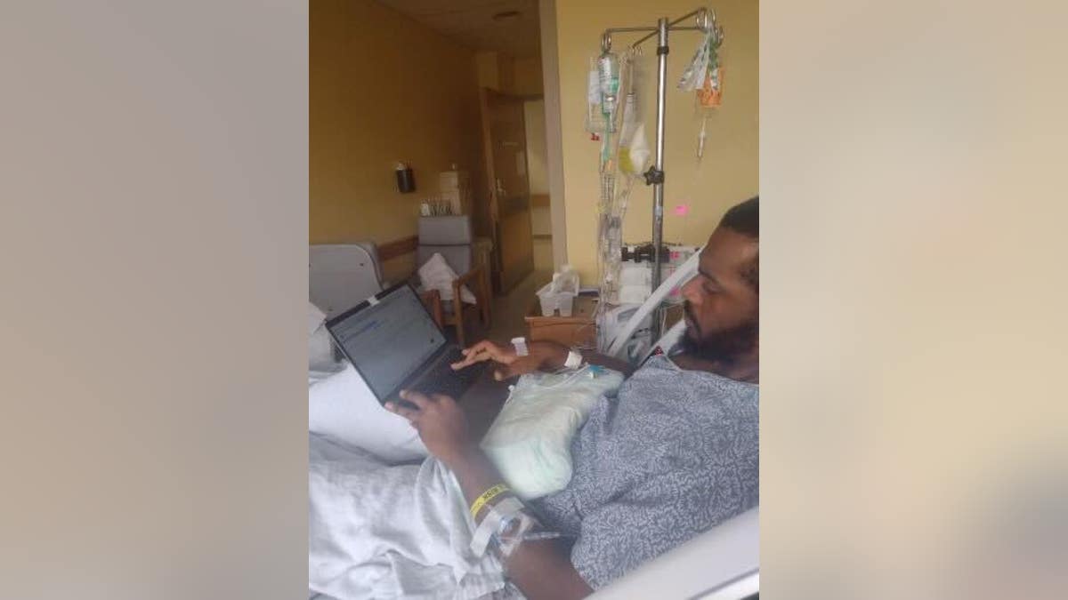 Raheem Bell working at a computer in a hospital bed