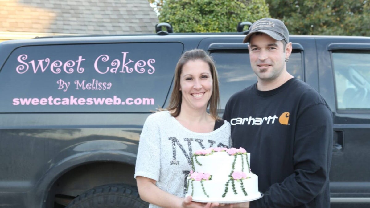 Melissa and Aaron Klein hold a cake in front of a vehicle marked "Sweet Cakes by Melissa"