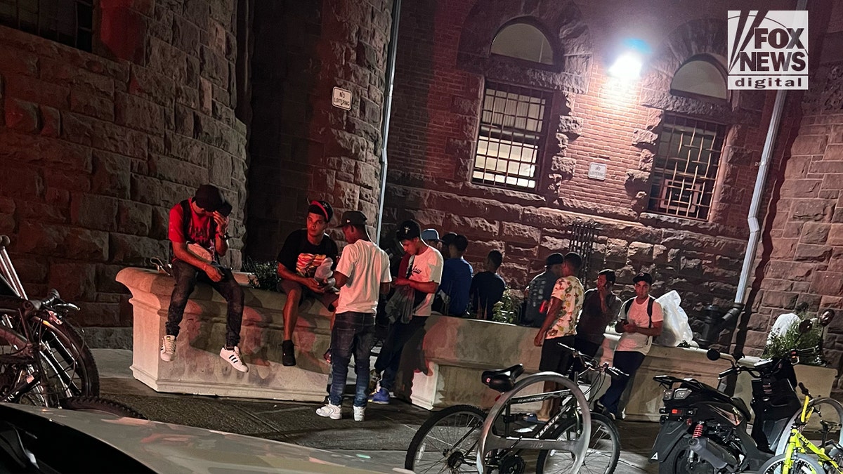 A dozen men, said to be newly arrived migrants, outside a brick building after dark