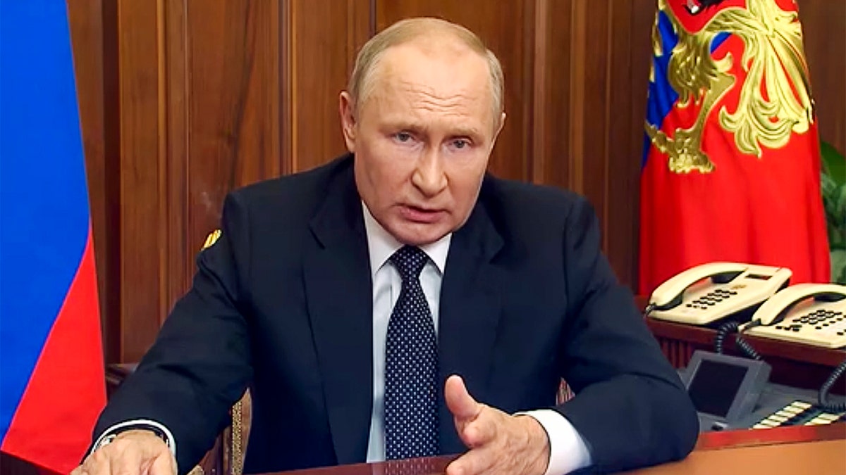 Russian President Vladimir Putin delivers address to the nation while wearing a dark suit and sitting at a desk