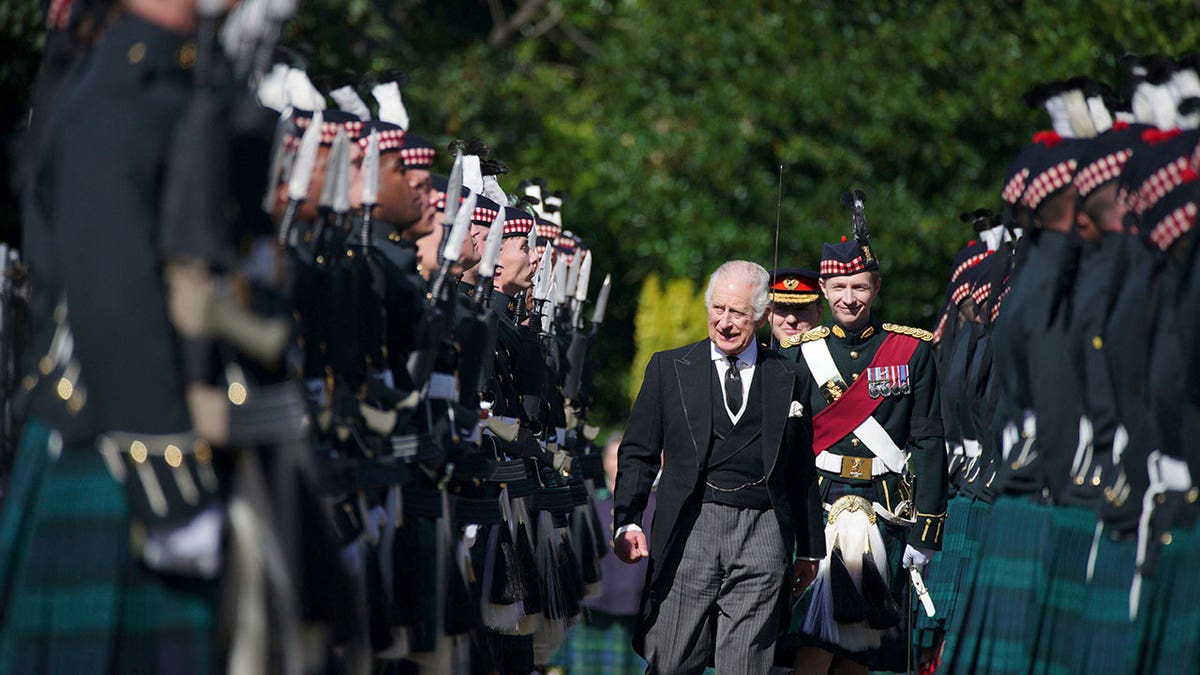 King Charles III wears a tailored suit as he walks down the line of guards during daytime