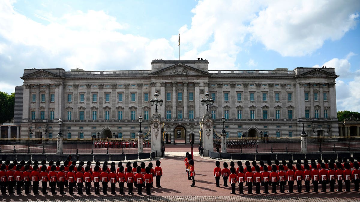 Guards dressed iin red uniform stand in front of Buckingham Palace
