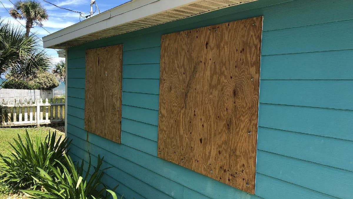 Turquoise paneled home has window boarded up with plywood