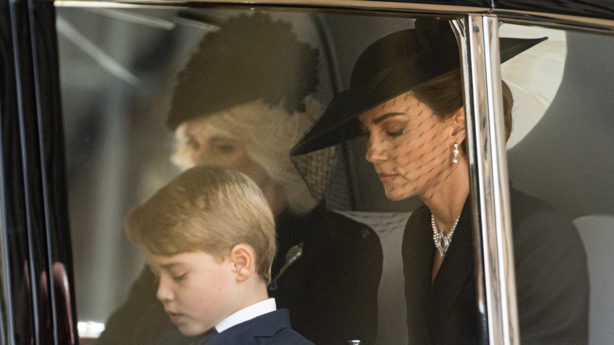 Kate Middleton, Camilla, and George look down as they drive in their car during Queen Elizabeth's state funeral