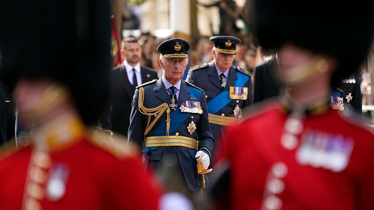 King Charles is dressed in military uniform as he follows behind guards and the Queen's coffin