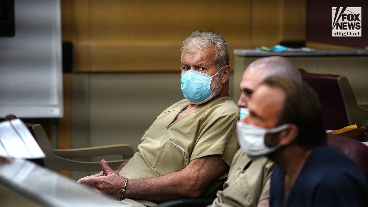 Louis Bianculli, wearing a surgical mask,stares at a cameraman from the defense table