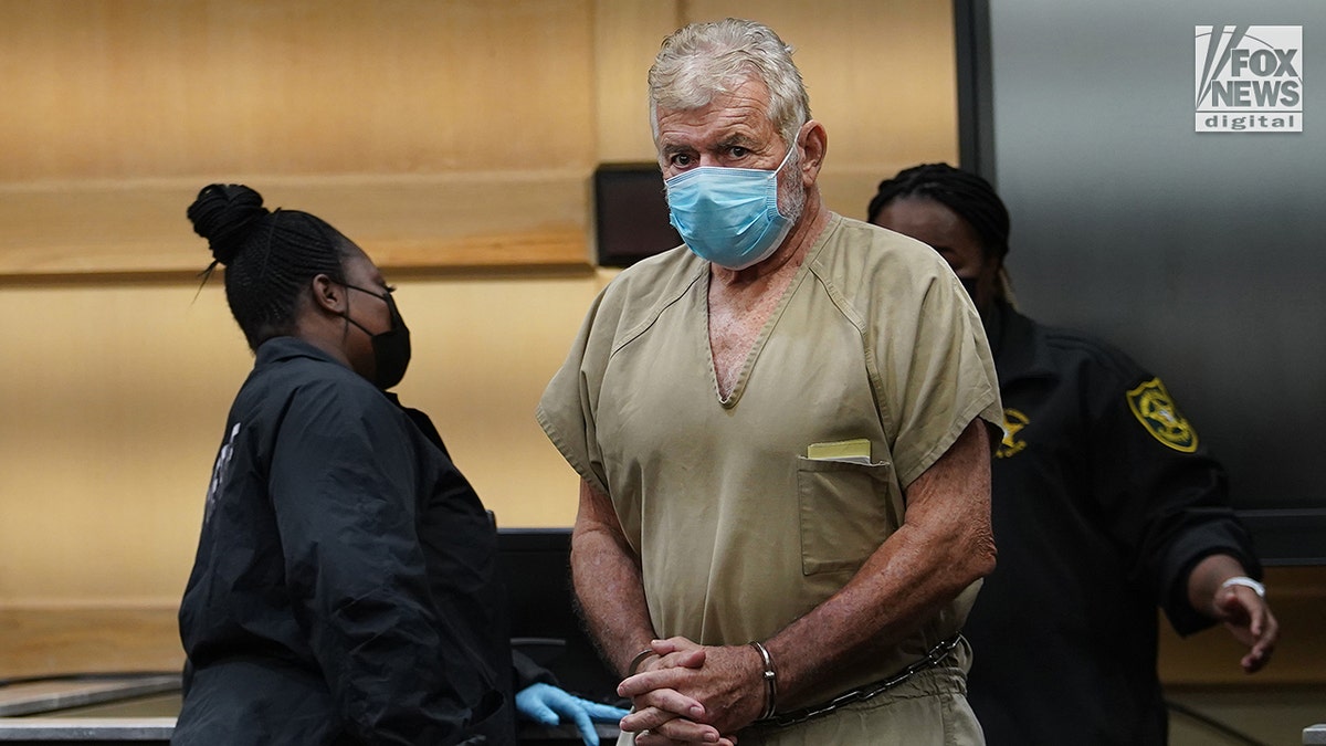 Bianculli standing in court in a beige jail-issue jumpsuit and wearing a blue surgical mask