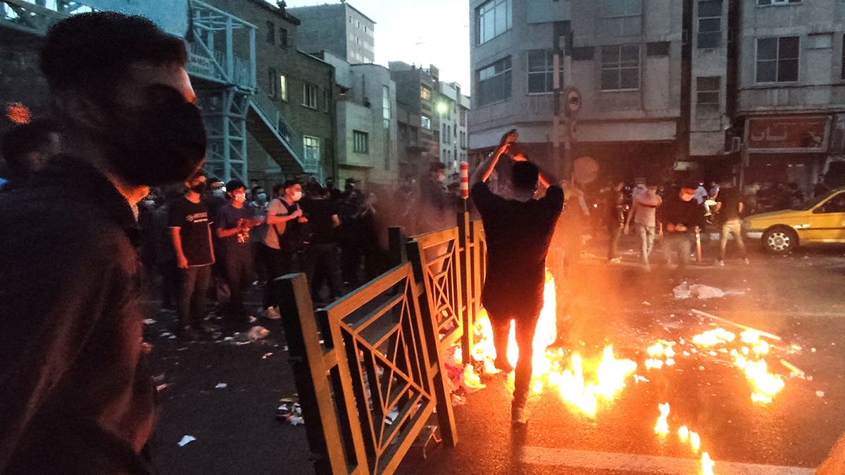 A man stands in front of a fire lit on a Tehran street as people protest