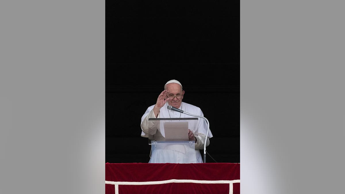 Pope Francis is outlined by a black background as he waves from a podium in the Vatican.