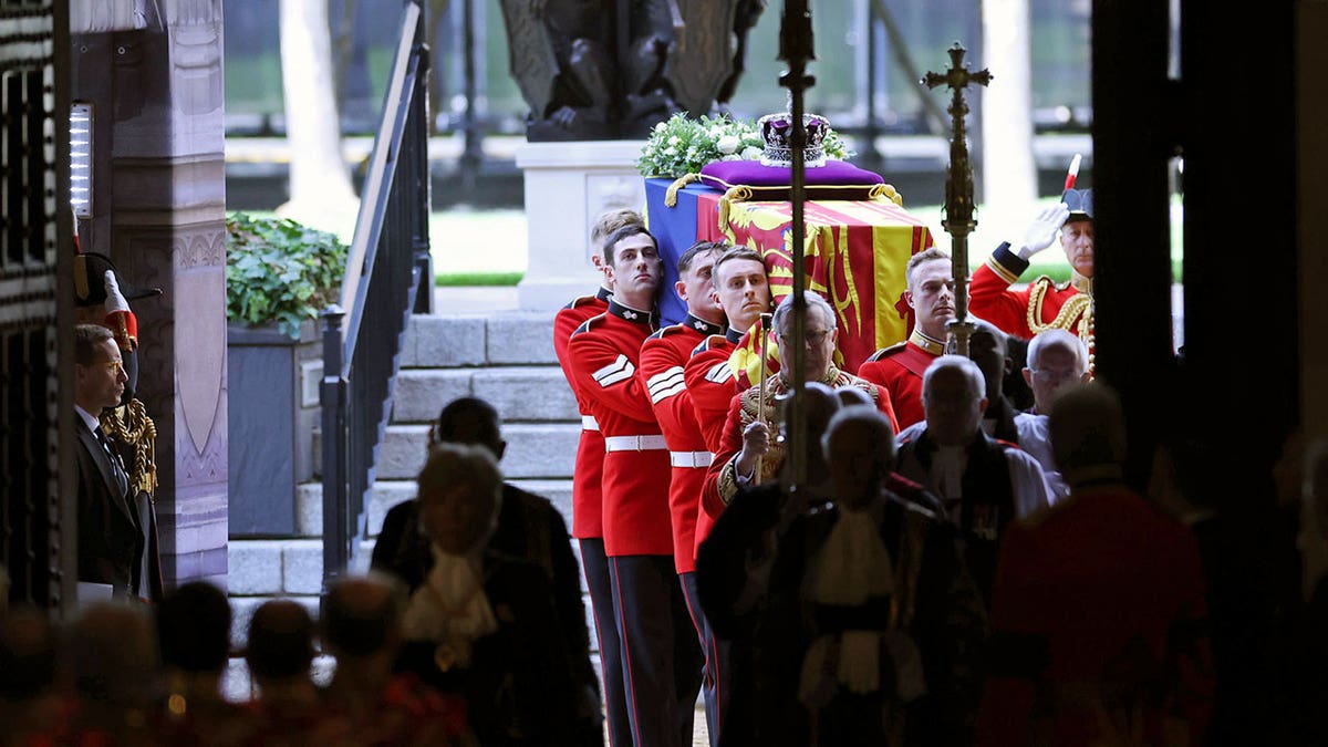 Queen Elizabeth's coffin is carried into a darkened building by guards in red uniforms