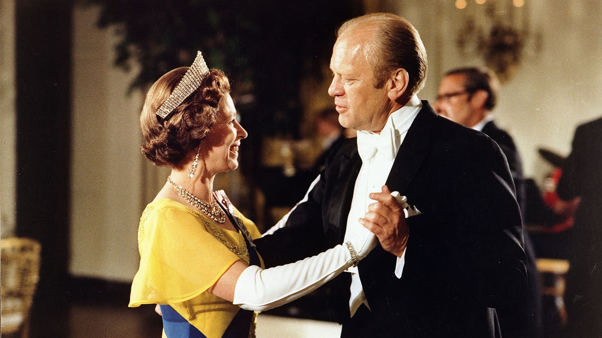 Queen Elizabeth wears a yellow dress and a crown while dancing with President Gerald Ford
