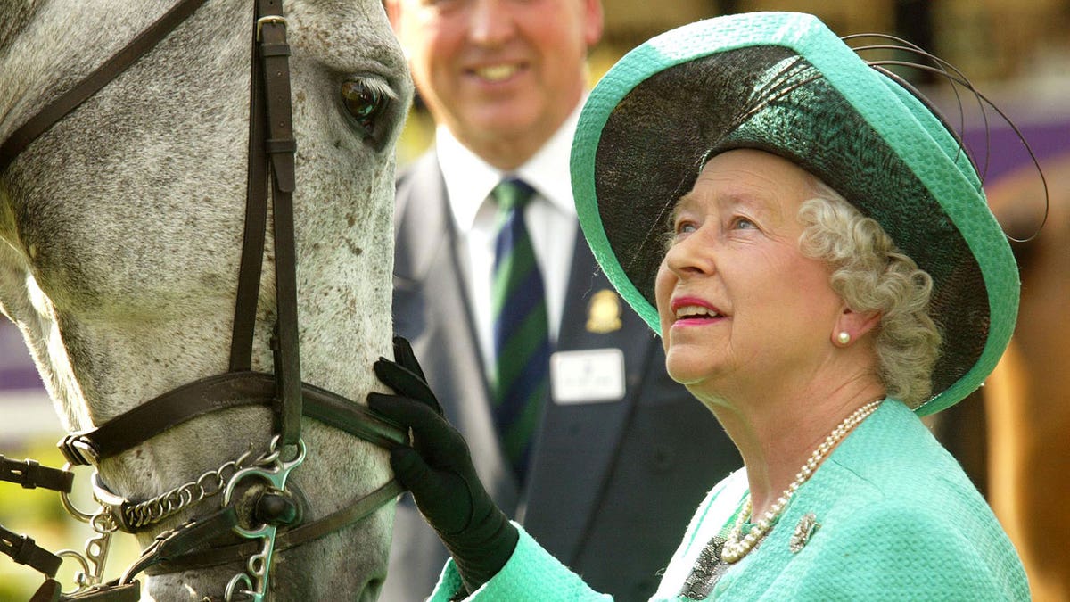 Queen Elizabeth wears a green dress and hat while petting a white horse