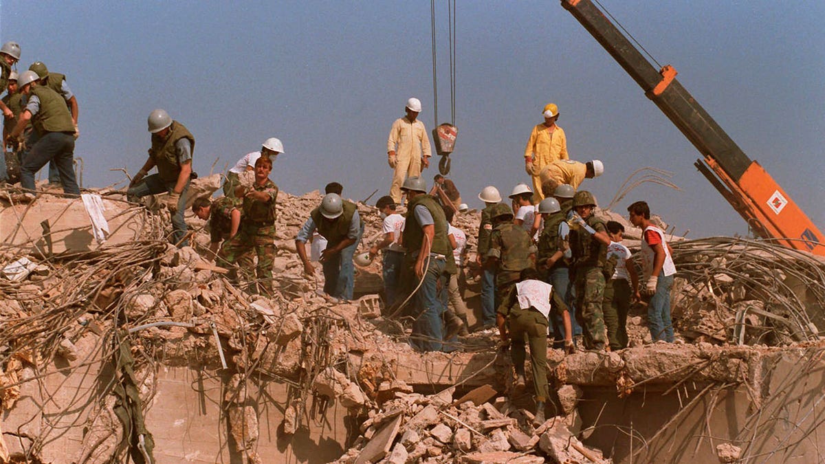 Rescue workers in hard hats and beige uniforms climb on rubble and rock