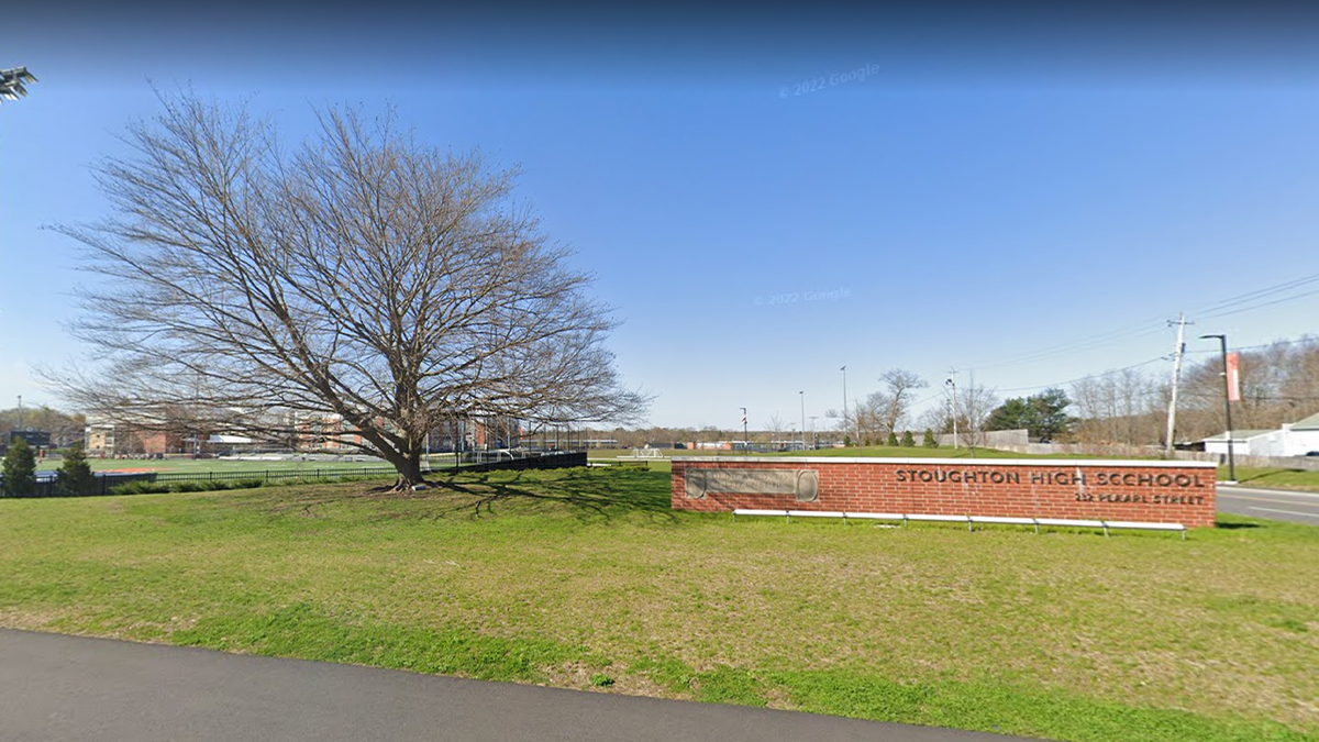 Photo shows entrance to Stoughton High in Mass. with sign in full view on bright, blue sky day