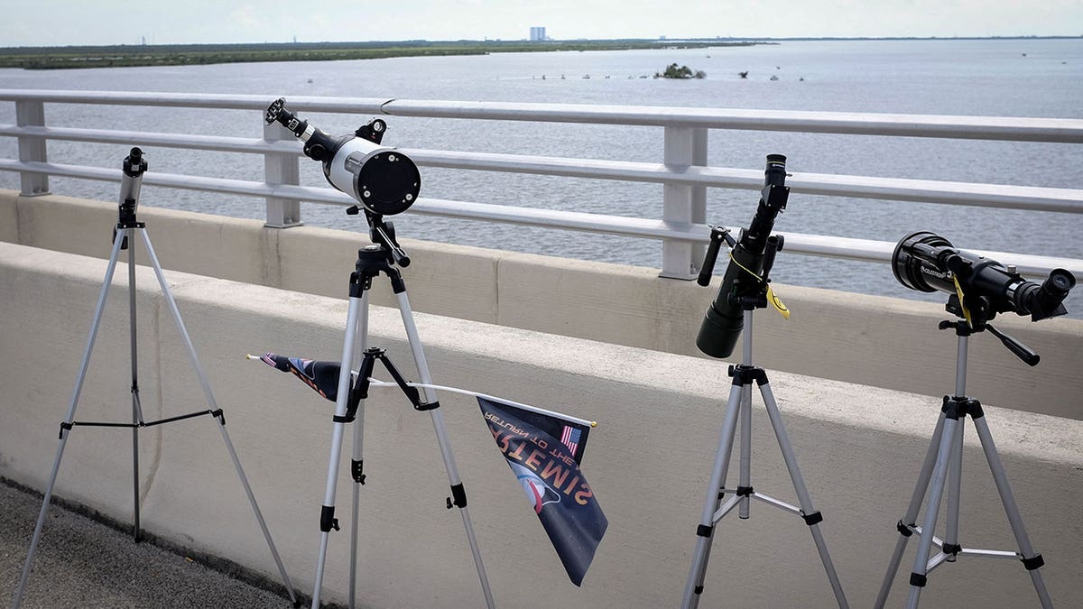 Telescopes are lined up on a balcony during daytime overlooking a body of water