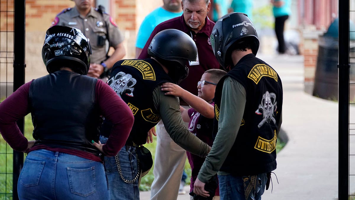 A student hugs an officer in uniform wearing a helmet and protective gear