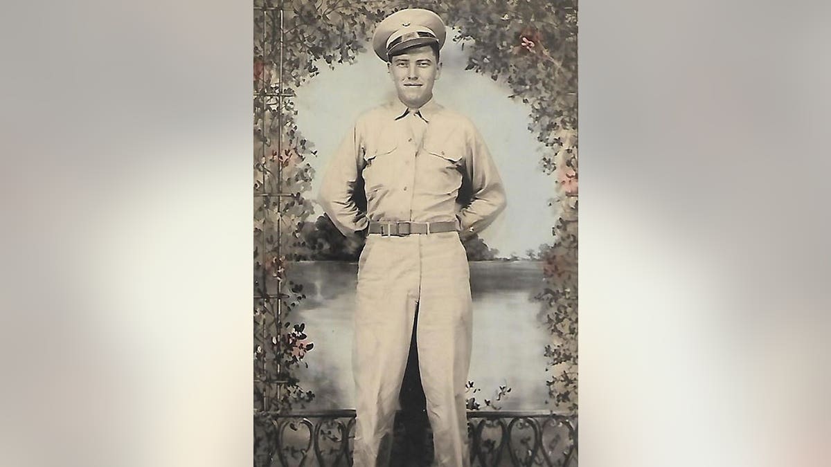 Soldier wears hat and army uniform in black and white photo with floral background behind him