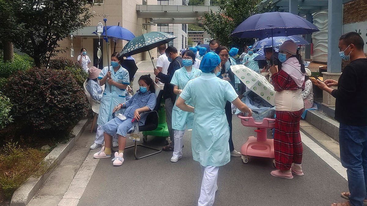 Ya'an residents with masks and umbrellas are gathered on a sidewalk during daytime