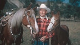 Country and western singer Gene Autry (1907-1998), dressed in cowboy hat and plaid shirt, poses with two horses, USA, circa 1955. Autry gained fame as 'The Singing Cowboy' on the radio, in movies and on television.