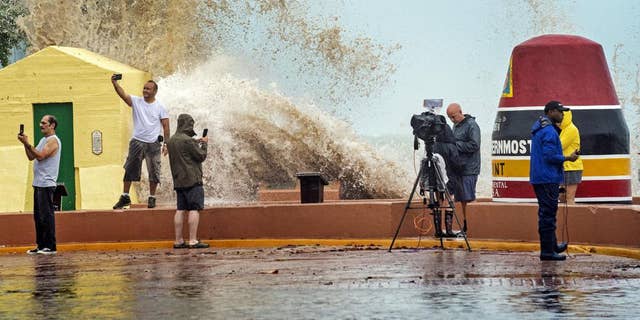 News crews, tourists and local residents take images as high waves from Hurricane Ian crash into the seawall at the Southernmost Point buoy, Tuesday, Sept. 27, 2022, in Key West, Fla.
