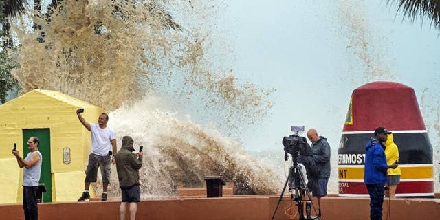 News crews, tourists and local residents take images as high waves from Hurricane Ian crash into the seawall at the Southernmost Point buoy, Tuesday, Sept. 27, 2022, in Key West, Fla.
