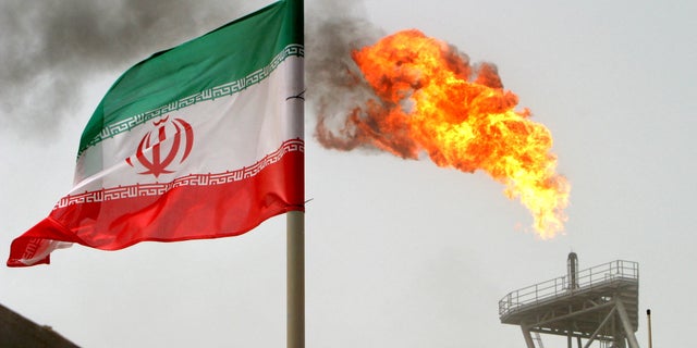 A gas flare on an oil production platform alongside an Iranian flag in the Gulf July 25, 2005. 