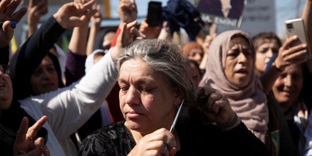 A woman cuts her hair during a protest over the death of 22-year-old Kurdish woman Mahsa Amini in Iran, in the Kurdish-controlled city of Qamishli, northeastern Syria September 26, 2022.  