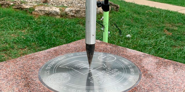 The tip of a tripod rests on the center of the 2020 Center of Population Commemorative Survey mark on Sept. 14, 2022, in Hartville, Missouri.