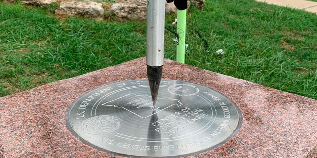 The tip of a tripod rests on the center of the 2020 Center of Population Commemorative Survey mark on Sept. 14, 2022, in Hartville, Missouri.