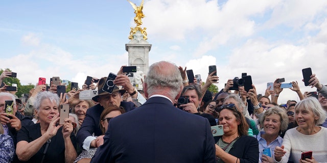 Britain's King Charles III, back to camera, greets well-wishers as he walks by the gates of Buckingham Palace.