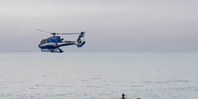 A helicopter flies overs an upturned boat with a survivor sitting on the hull off the coast of Kaikoura, New Zealand, Saturday, Sept. 10, 2022. 