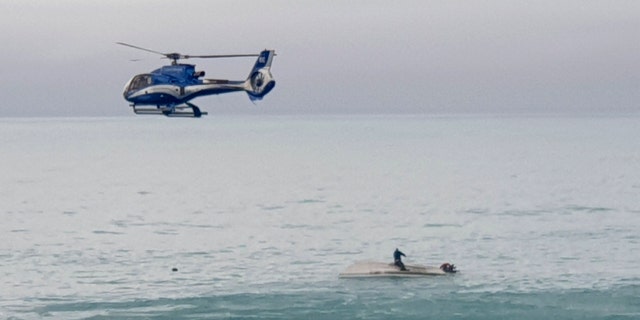 A helicopter flies overs an upturned boat with a survivor sitting on the hull off the coast of Kaikoura, New Zealand, Saturday, Sept. 10, 2022. 