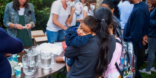 A woman, who is part of a group of immigrants that had just arrived, holds a child as they are fed outside St. Andrews Episcopal Church, Wednesday Sept. 14, 2022, in Edgartown, Mass., on Martha's Vineyard. 