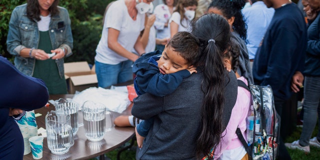 A woman, who is part of a group of immigrants that had just arrived, holds a child as they are fed outside St. Andrews Episcopal Church, Wednesday Sept. 14, 2022, in Edgartown, Mass., on Martha's Vineyard.