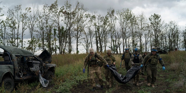 Ukrainian national guard servicemen carry a bag containing the body of a Ukrainian soldier in an area near the border with Russia, in Kharkiv region, Ukraine, Monday, Sept. 19, 2022.