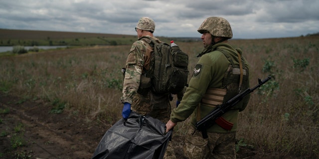 Ukrainian national guard servicemen carry a bag containing the body of a Ukrainian soldier in an area near the border with Russia, in Kharkiv region, Ukraine, Monday, Sept. 19, 2022. 