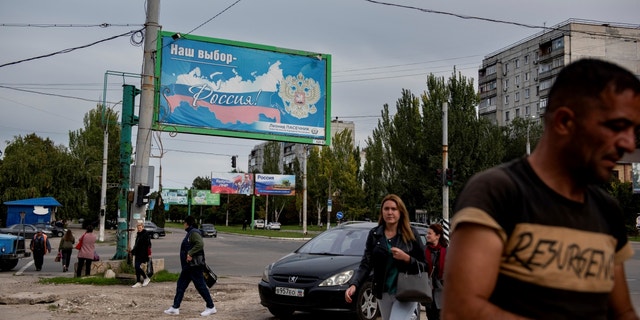 People walk in a street with a billboard that reads: "Our choice - Russia", prior to a referendum in Luhansk, Luhansk People's Republic controlled by Russia-backed separatists, eastern Ukraine, Sept. 22, 2022.