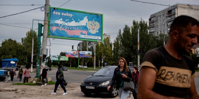 People walk in a street with a billboard that reads: "Our choice - Russia", prior to a referendum in Luhansk, Luhansk People's Republic controlled by Russia-backed separatists, eastern Ukraine, Sept. 22, 2022.