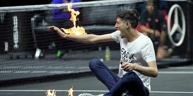 A man sets fire on his hand during protest at a match Team World's Diego Schwartzman against Team Europe's Stefanos Tsitsipas on day one of the Laver Cup tennis tournament at the O2 in London, Friday, Sept. 23, 2022. 