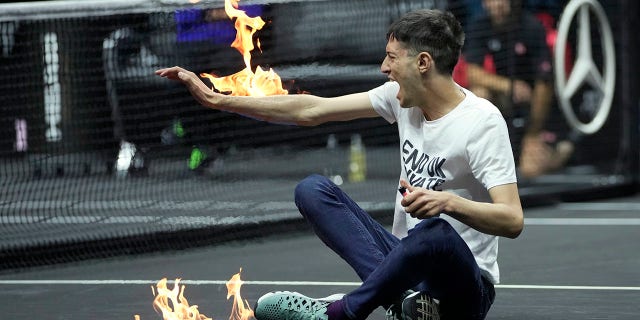 A man sets fire on his hand during protest at a match Team World's Diego Schwartzman against Team Europe's Stefanos Tsitsipas on day one of the Laver Cup tennis tournament at the O2 in London, Friday, Sept. 23, 2022.