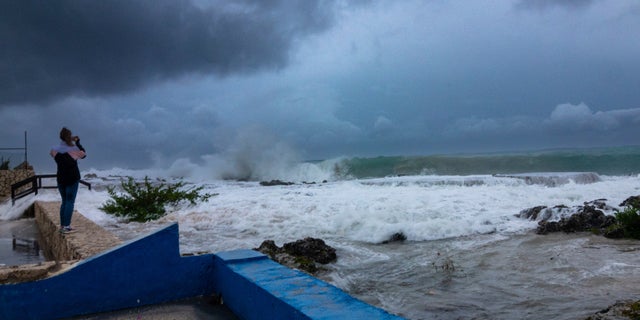 A woman takes photos while waves crash against a seawall as Hurricane Ian passes through George Town, Grand Cayman island, Monday, Sept. 26, 2022. Hurricane Ian is on a track to hit the west coast of Florida as a major hurricane as early as Wednesday.