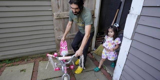 Mohammad Walizada, left, who fled Afghanistan with his family, assists his daughter Hasnat, 3, with a bicycle at their home in Epping, N.H., Thursday, Sept. 15, 2022. Since the U.S. military’s withdrawal from Kabul last year, the Sponsor Circle Program for Afghans has helped over 600 Afghans restart their lives in their communities. (AP Photo/Steven Senne)