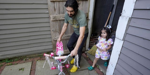 Mohammad Walizada, left, who fled Afghanistan with his family, assists his daughter Hasnat, 3, with a bicycle at their home in Epping, N.H., Thursday, Sept. 15, 2022. Since the U.S. military’s withdrawal from Kabul last year, the Sponsor Circle Program for Afghans has helped over 600 Afghans restart their lives in their communities. (AP Photo/Steven Senne)