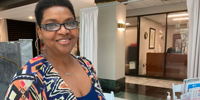 Amanda Rouser poses for a photo in front of a recruiting desk for new poll workers at Atlanta City Hall on Sept. 14, 2022, in Atlanta. Rouser was motivated to serve as a poll worker for the first time during the upcoming midterm election by false allegations of fraud against a Georgia poll worker after the 2020 presidential election. (AP Photo/Sudhin Thanawala)