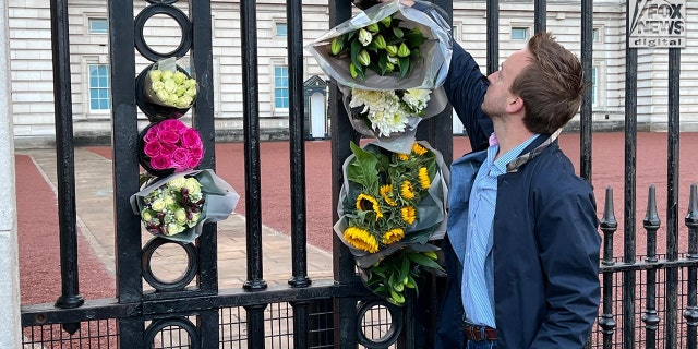 A man places flowers in between the gates outside Buckingham Palace as the news that Queen Elizabeth II has died today, September 8, 2022.