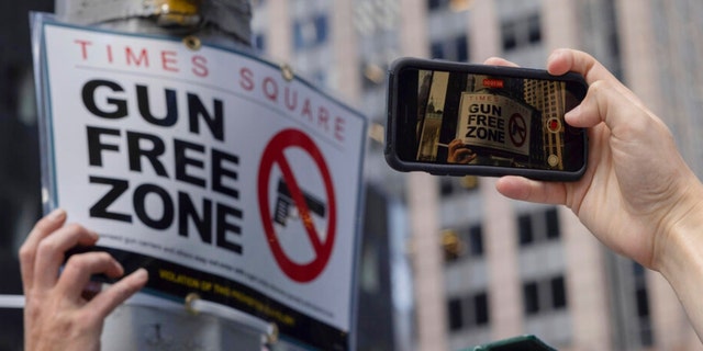 A person takes picture of an New York Police Department public affairs officer setting up signs reading Gun Free Zone around Times Square in New York on Wednesday, Aug. 31, 2022. 