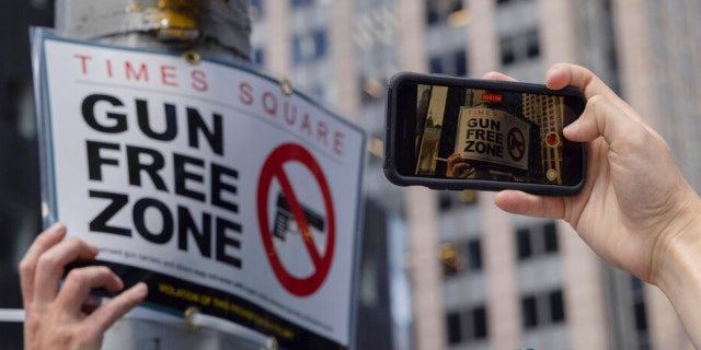 A person takes picture of an New York Police Department public affairs officer setting up signs reading Gun Free Zone around Times Square in New York on Wednesday, Aug. 31, 2022.